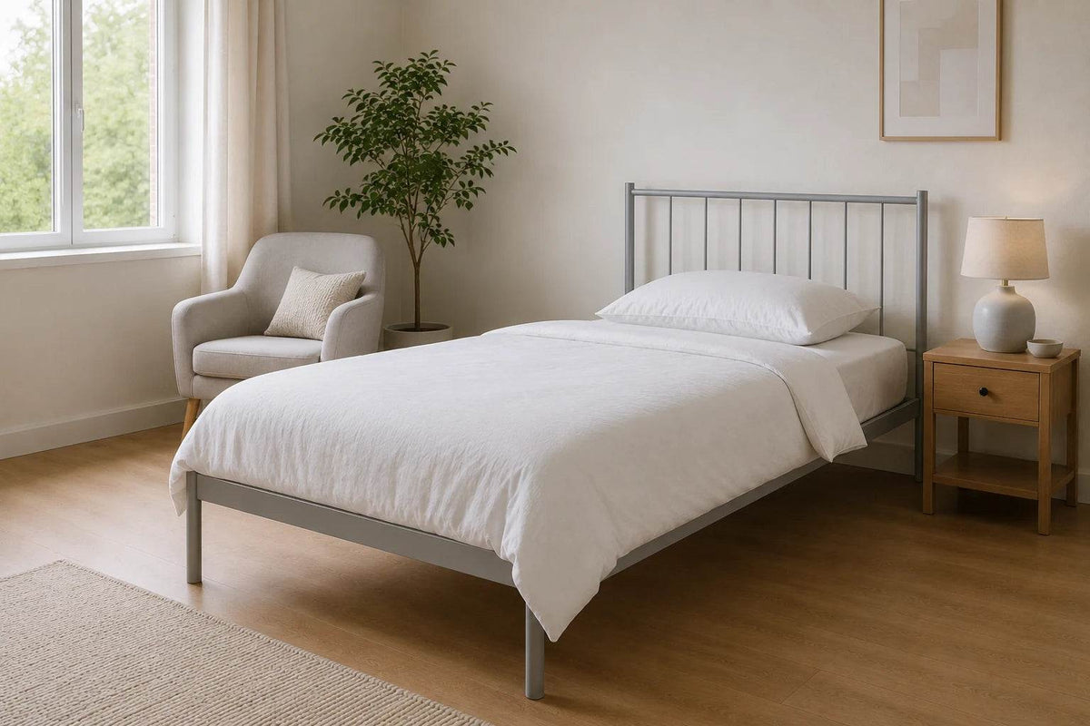 Metallbett 100 x 200 cm in silbergrau in einem ruhigen, hellen Schlafzimmer mit Lesesessel, weißer Bettwäsche und viel Bewegungsfläche